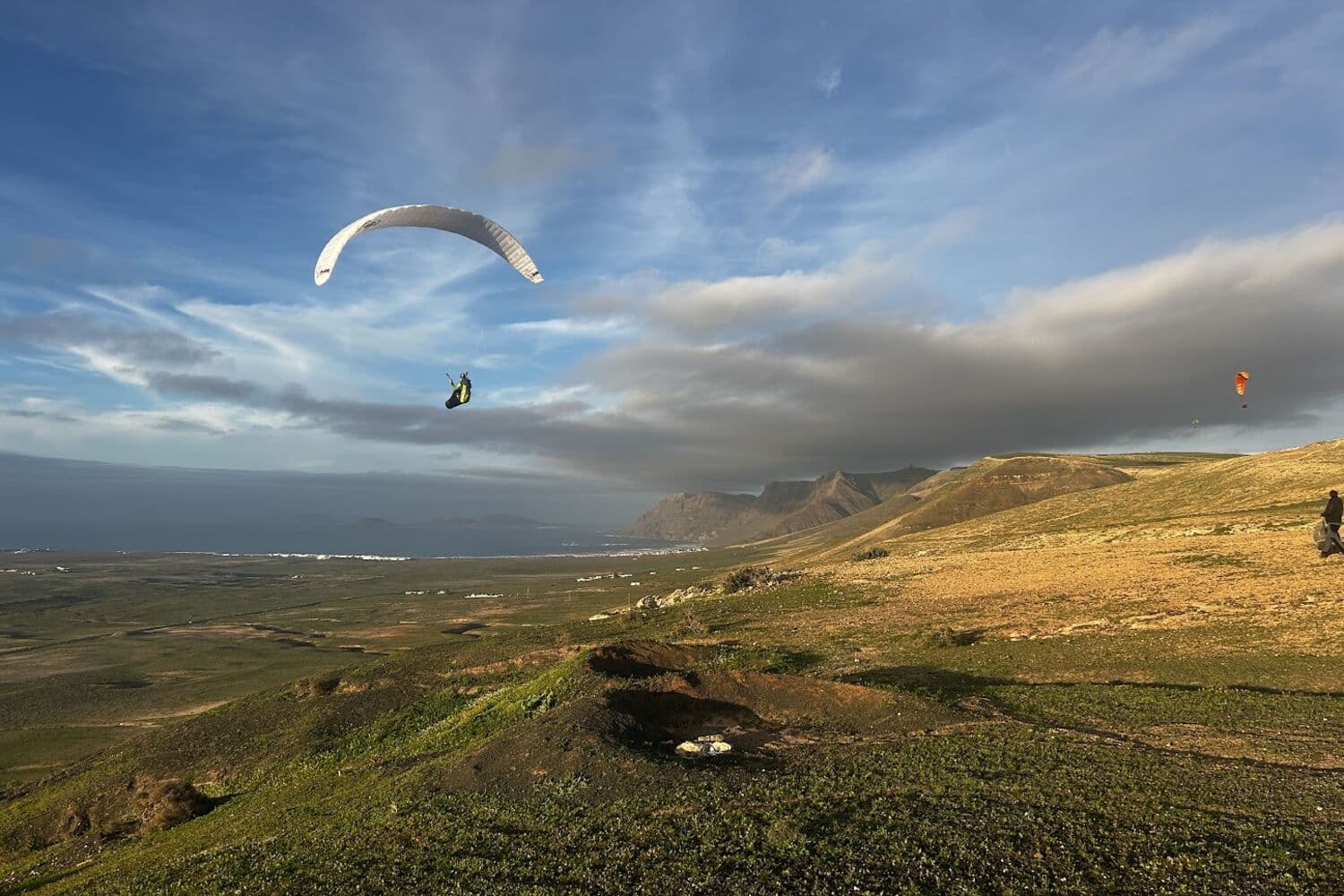A paraglider over the green slopes of Los Pechos, above the Famara cliffs in Lanzarote