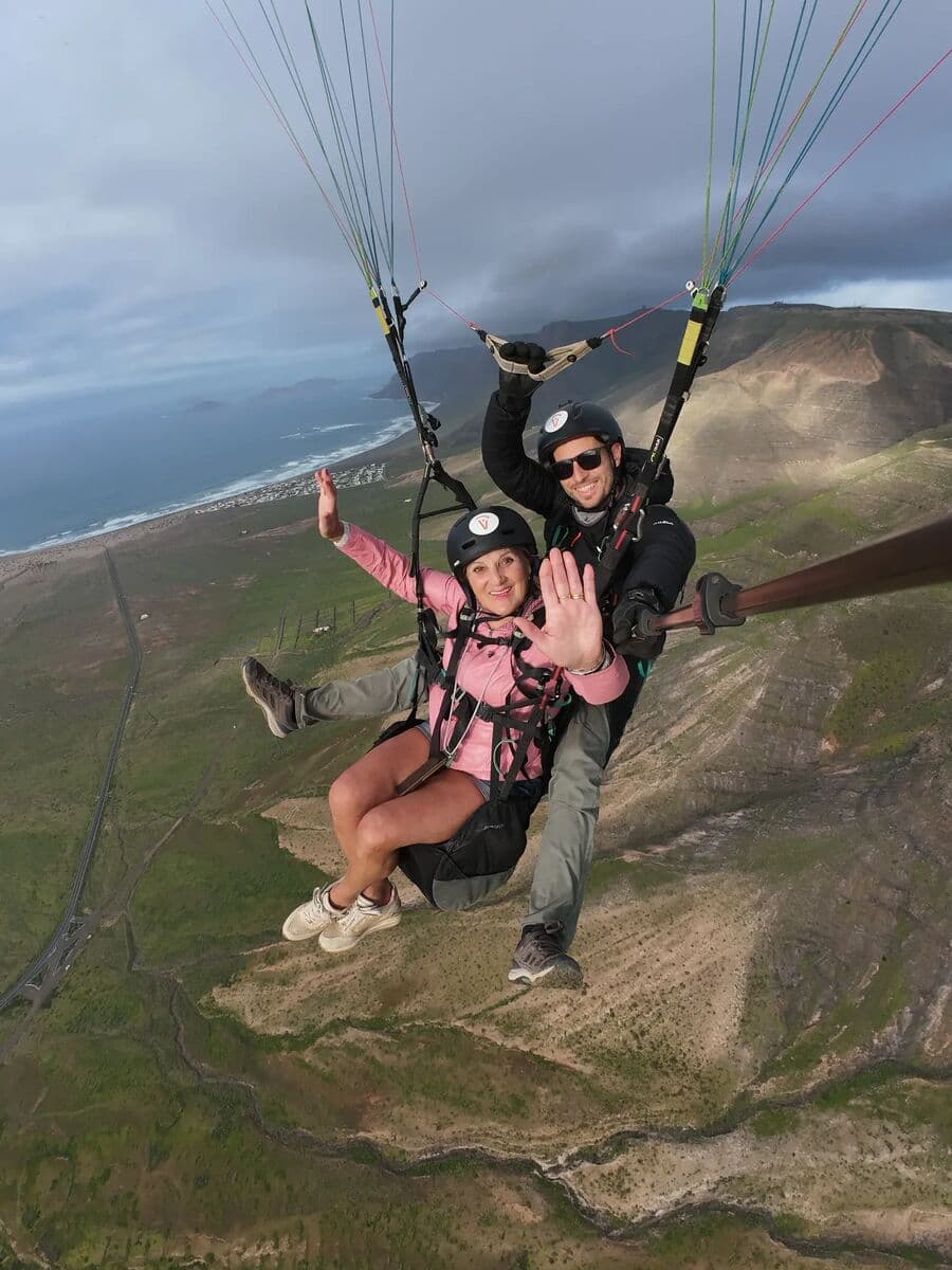 A tandem passenger waving over Los Pechos, with the coast below