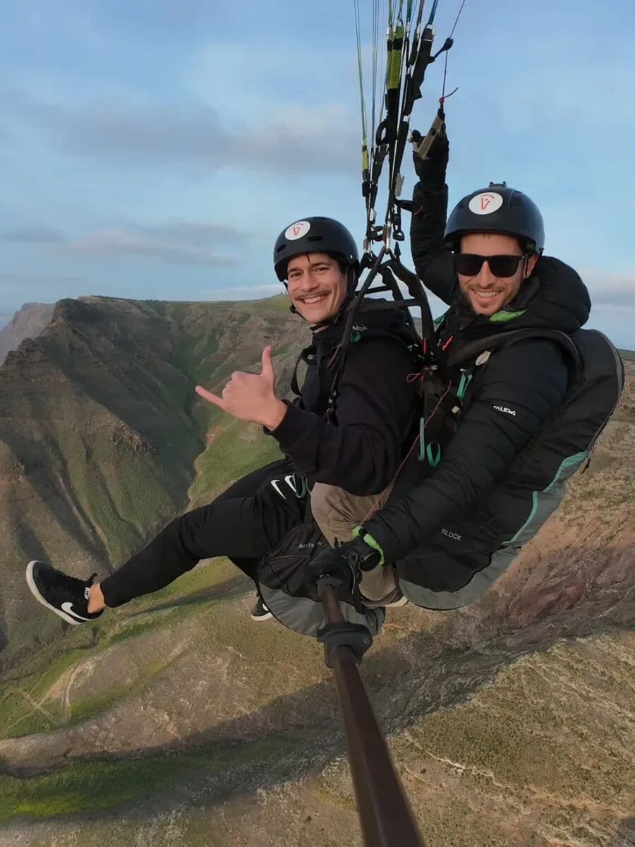 A tandem pilot and passenger making a shaka sign above the Famara cliffs
